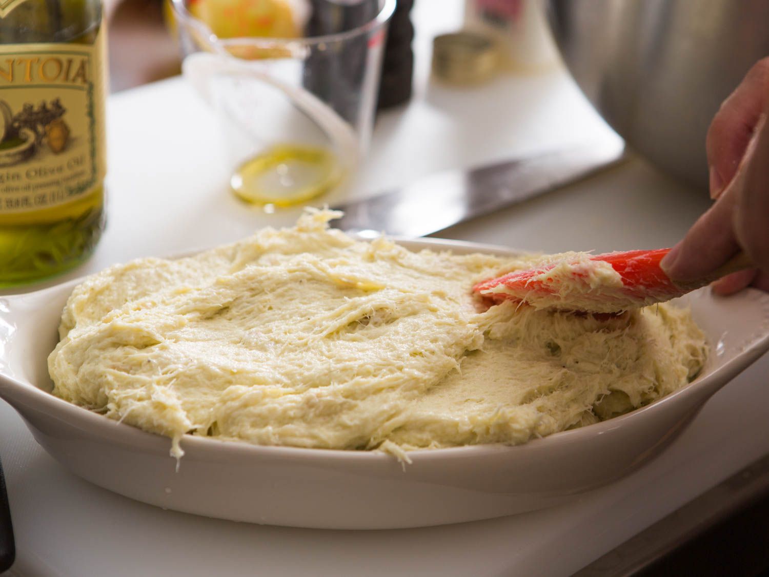 Spreading the mixed brandade into a shallow baking dish with a red silicone spatula.