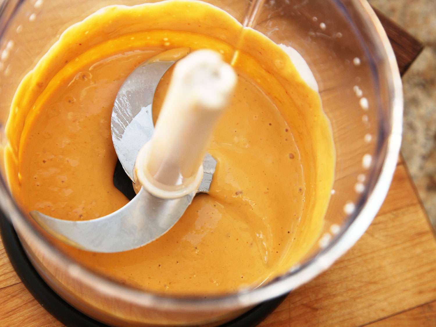 Overhead shot of an open food processor containing uni (sea urchin) and Mexican crema, blended to a smooth orange purée.