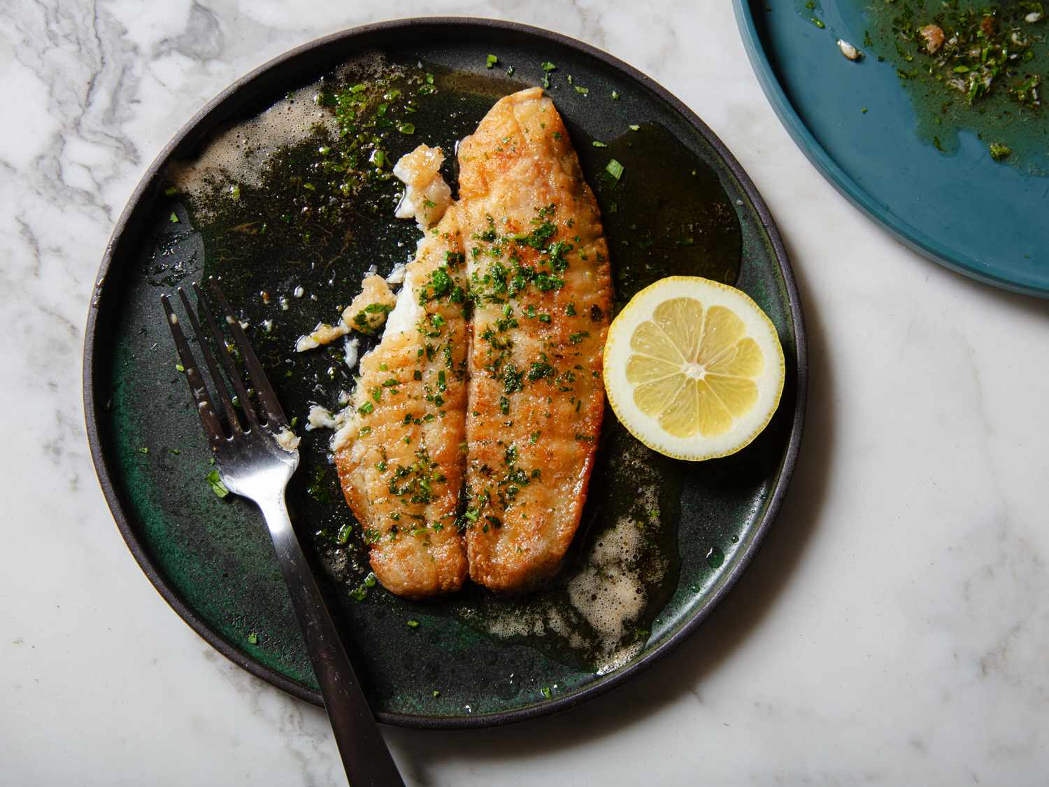 Overhead view of sole meuniere, half eaten with a fork resting on the plate.