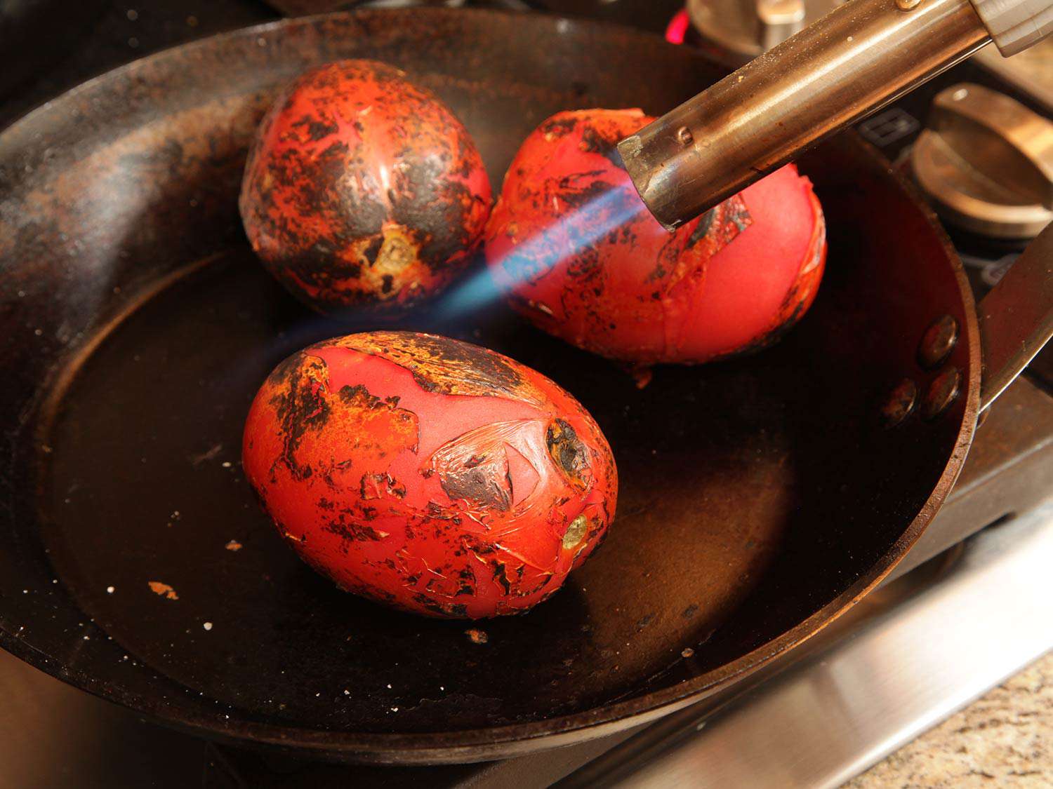 Charring three roma tomatoes in a skillet with a culinary blow torch