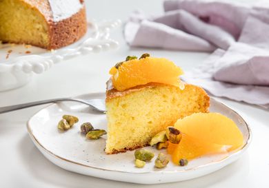 A slice of olive oil cake topped with orange segments and pistachios.