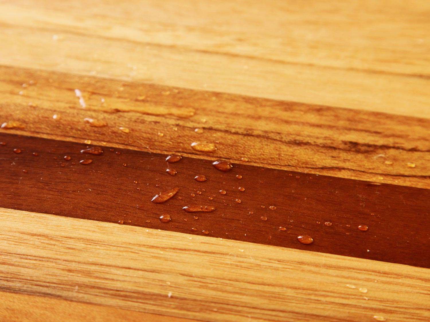 Closeup of water beading on the surface of a cutting board.