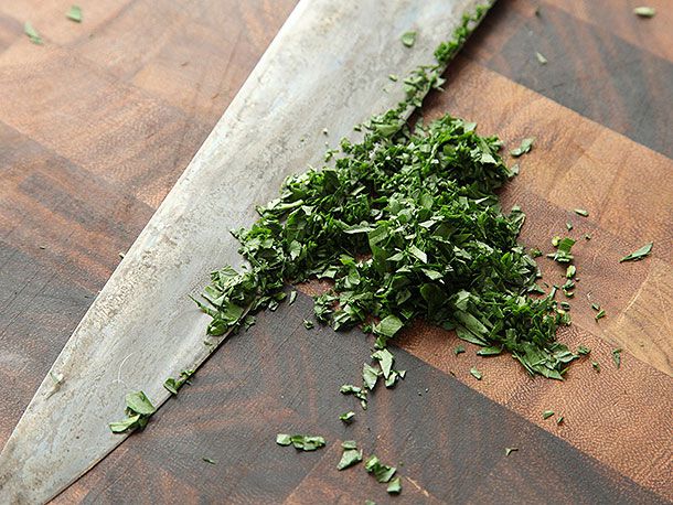 A knife resting with a pile of minced herbs on a cutting board.