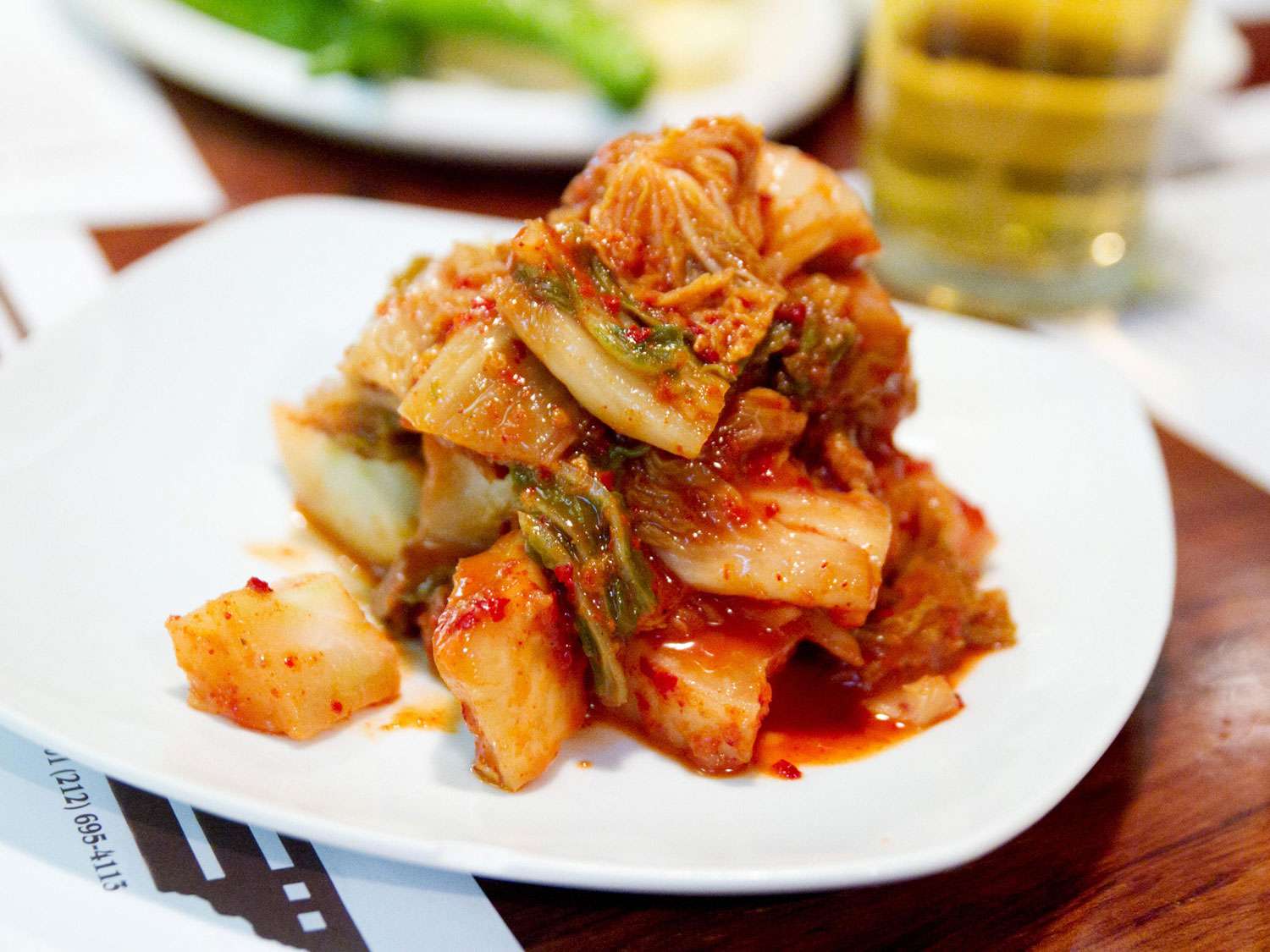 A mound of kimchi on a while plate on a dining table.