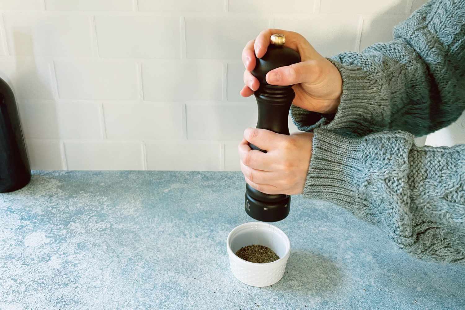 a person grinding pepper into a small ramekin