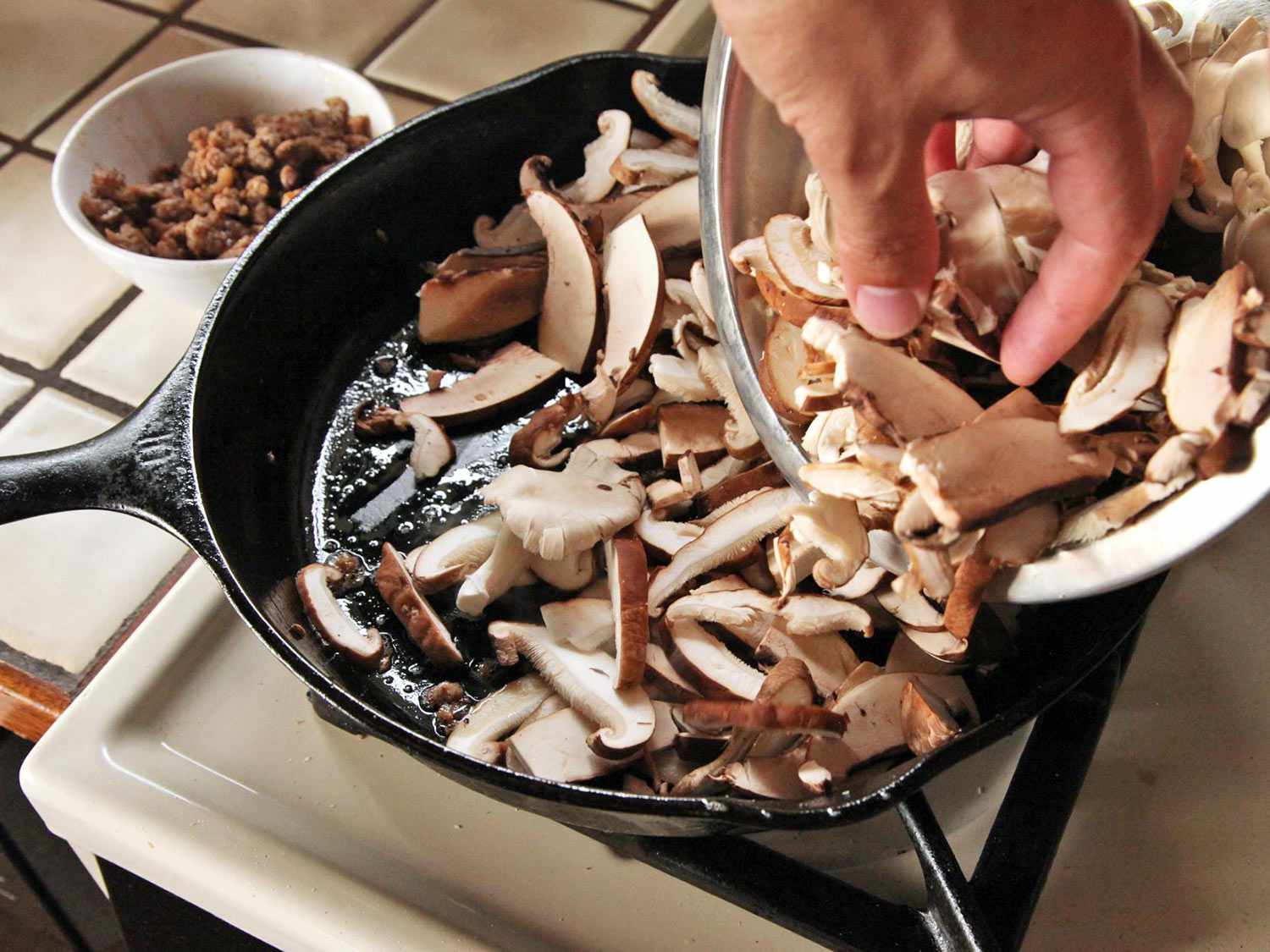 Adding mushrooms to sausage fat in a cast iron skillet..
