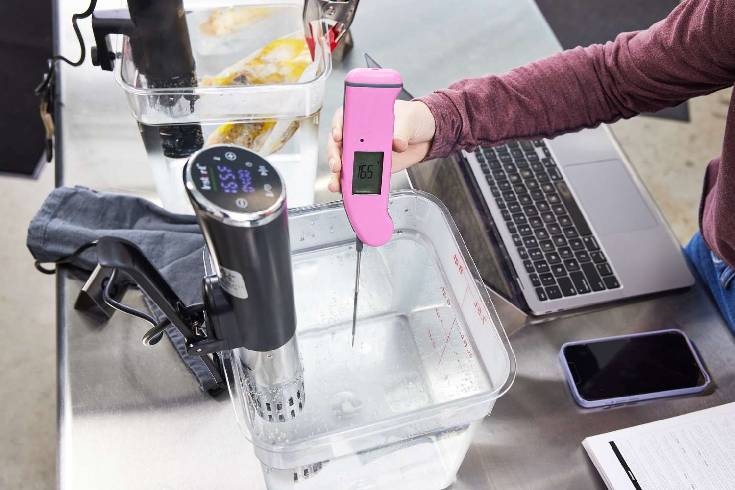 Hand holding a thermometer in a bucket of water being heated by the Instant Accu Slim Sous Vide Immersion Circulator