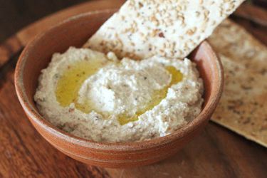 Sprouted chickpea hummus in a bowl, drizzled with olive oil with a seeded cracker in a bowl.