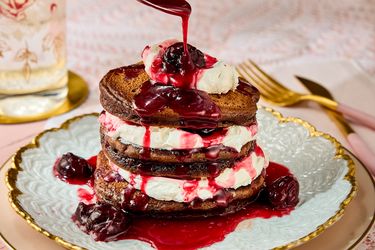 Stack of pancakes layered with cream and topped with berry sauce on a decorative plate