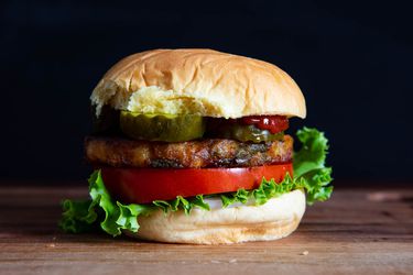 A fully dressed veggie burger on a bun with pickle, tomato, and lettuce.