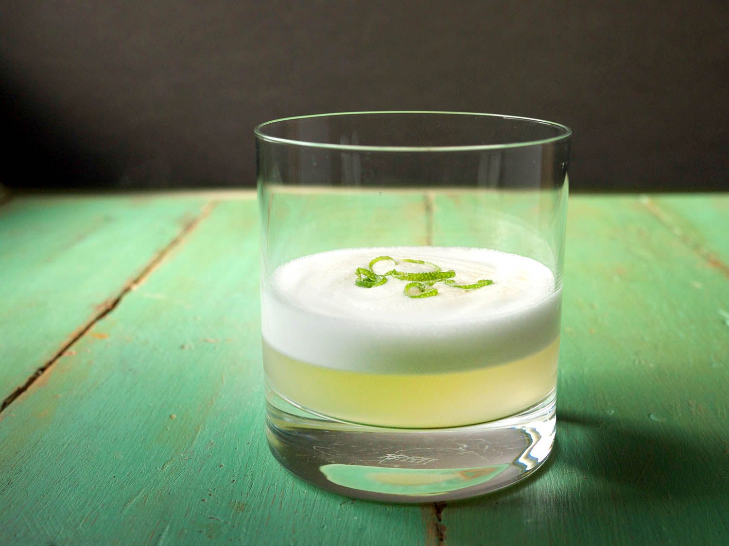 A lemongrass sour garnished with lime zest on a green wooden surface.