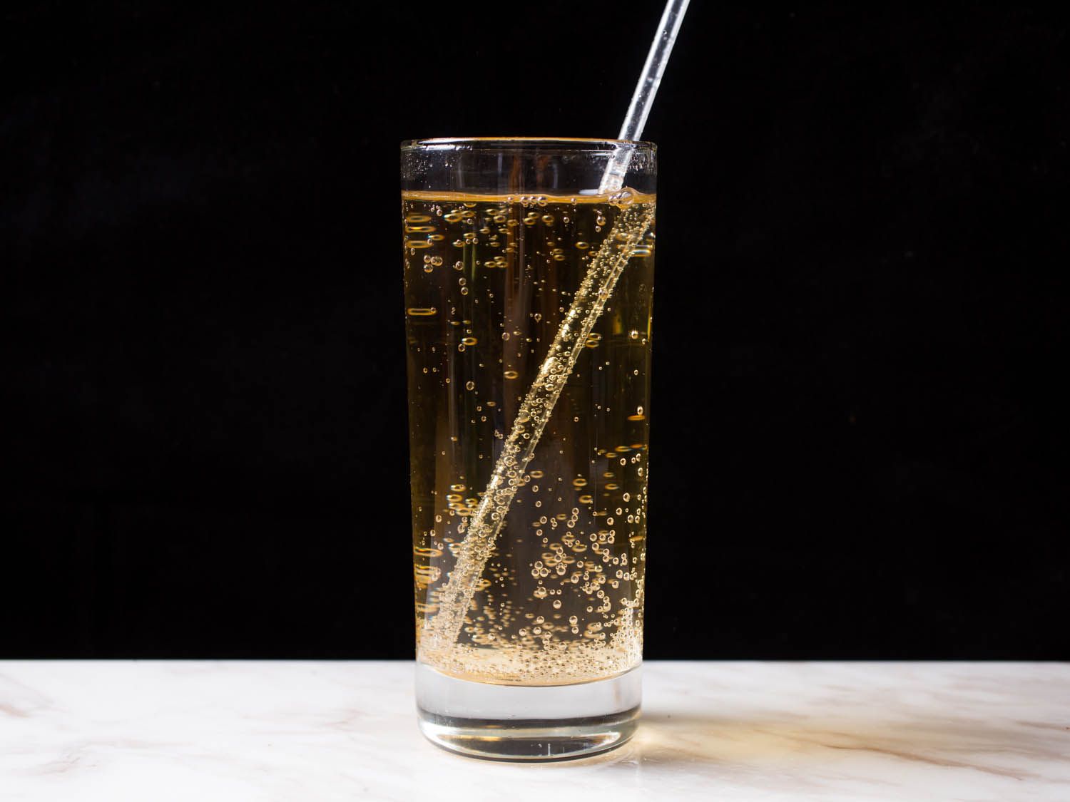 A tall glass filled with Dr. Brown's Cel-Ray soda, with a straw in the glass.