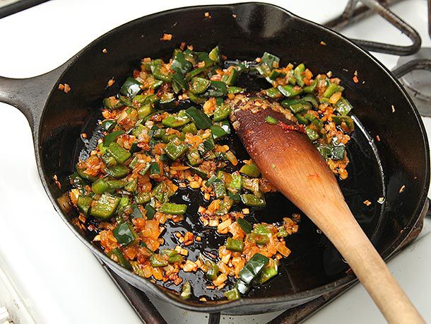 Sauteeing chopped onions and poblano peppers in a cast iron skillet. 