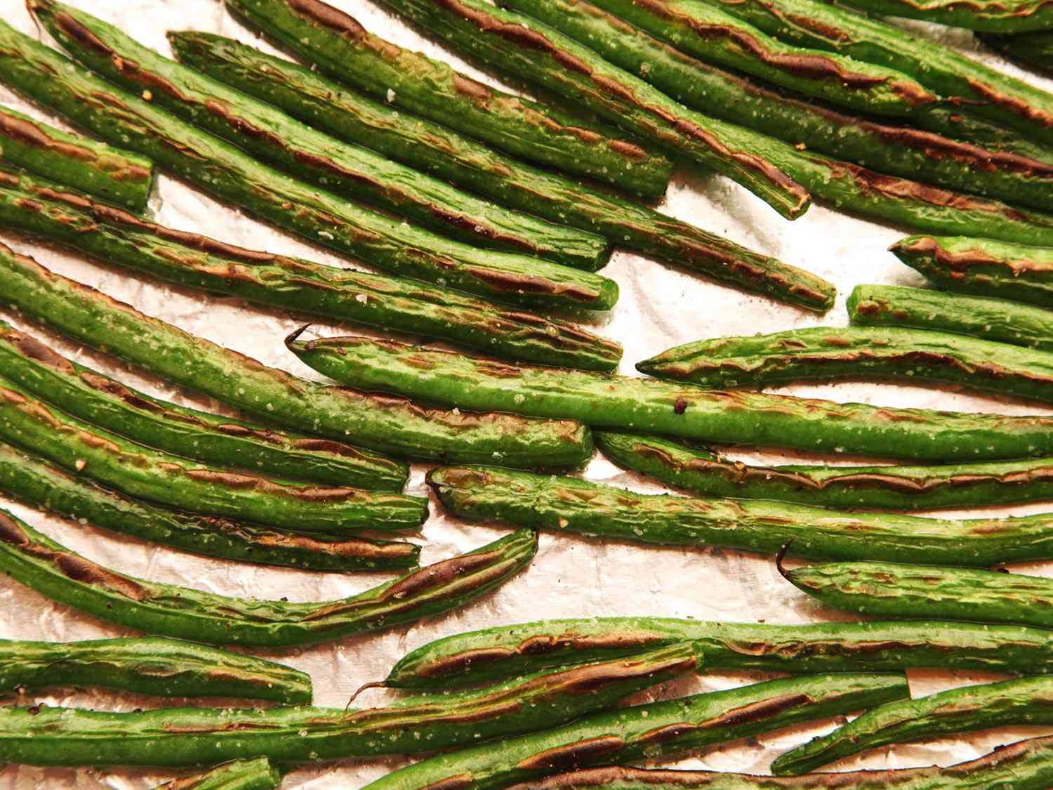 Overhead view of broiled green beans on a foil-lined baking sheet. They are lightly browned.