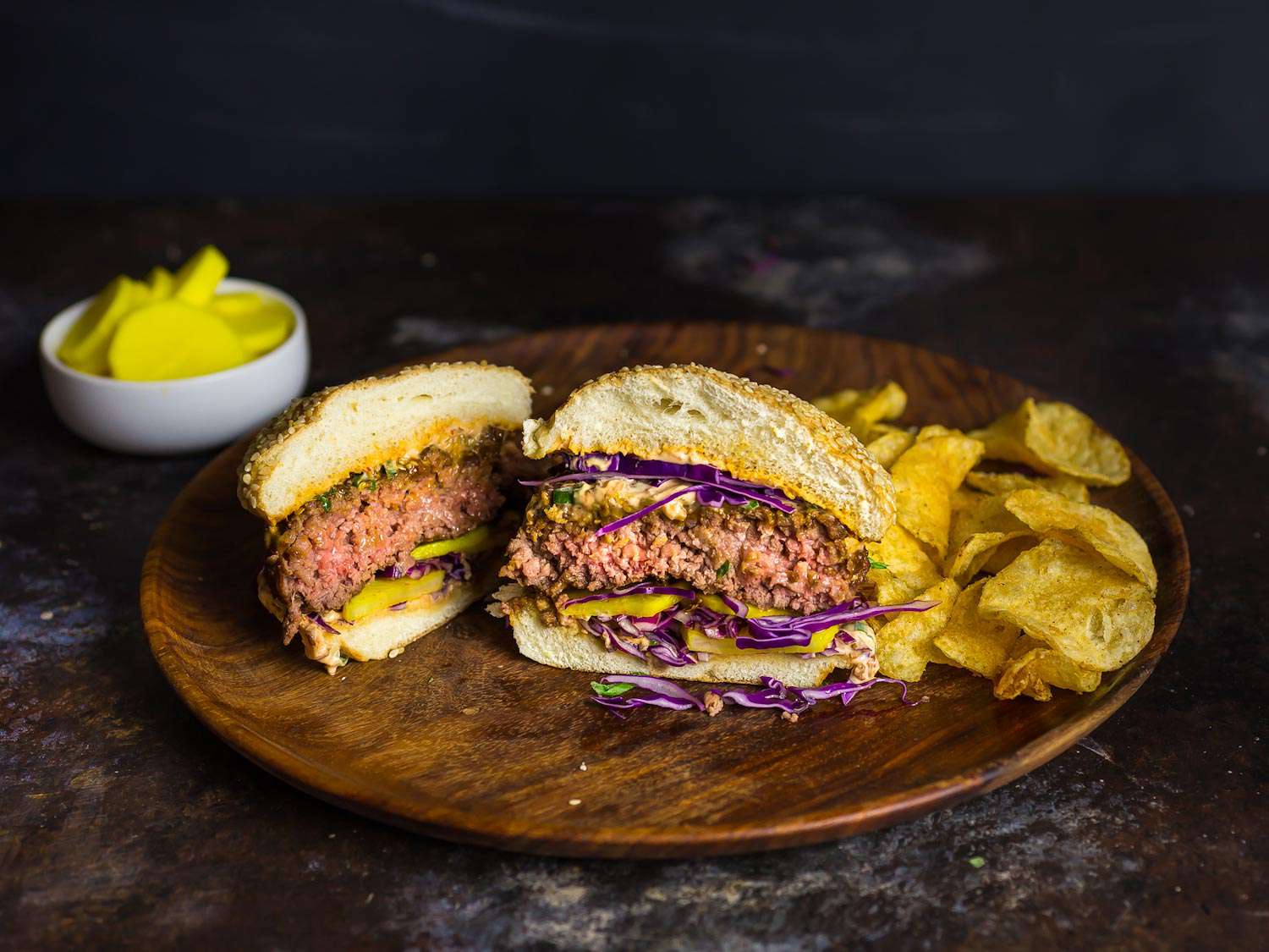 Cross section of a bulgogi burger on a serving plate with potato chips. On the background is danmuji (Korean pickled daikon radish) 