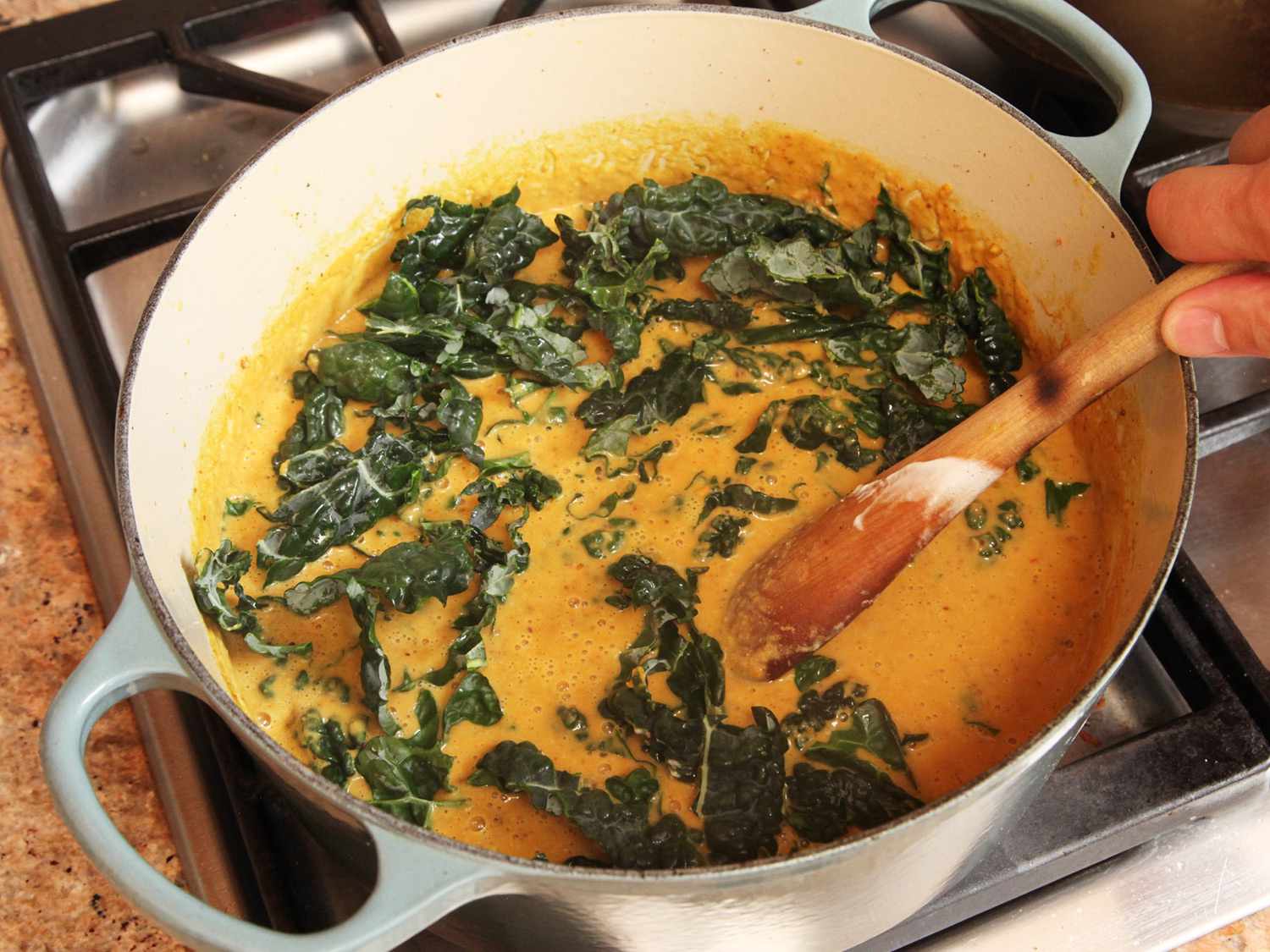 Stirring chopped kale into peanut soup.