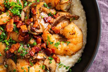 A dish featuring shrimp diced bacon mushrooms and garnish over a creamy base served in a bowl