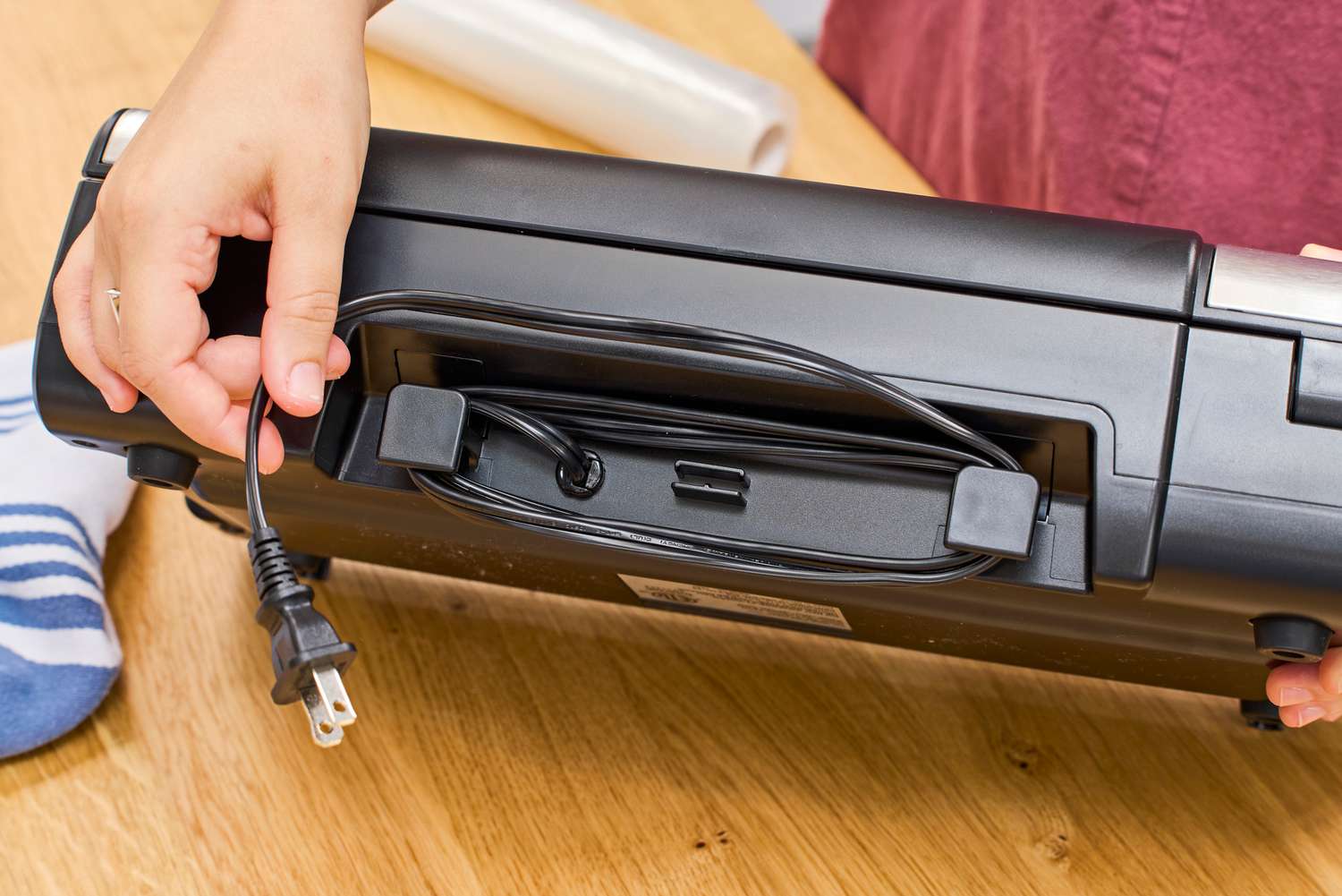 A person winds the power cord on the Nesco VS-12 Deluxe Vacuum Sealer