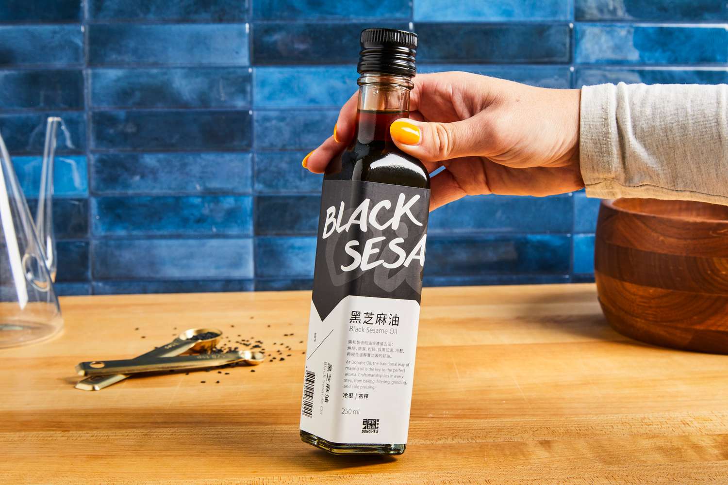 A person holding a bottle labeled "Black Sesame Oil" in a kitchen setting