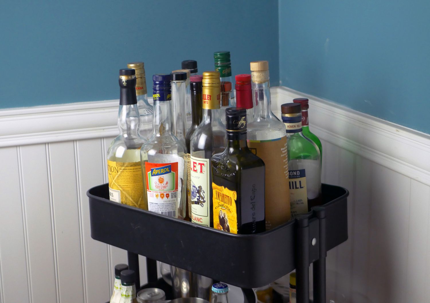 Numerous liquor bottles on the top shelf of a bar cart.