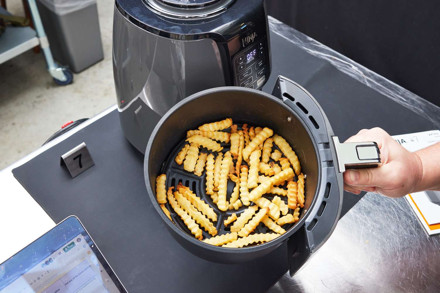 A person pulling on an air fryer's basket filled with fries.