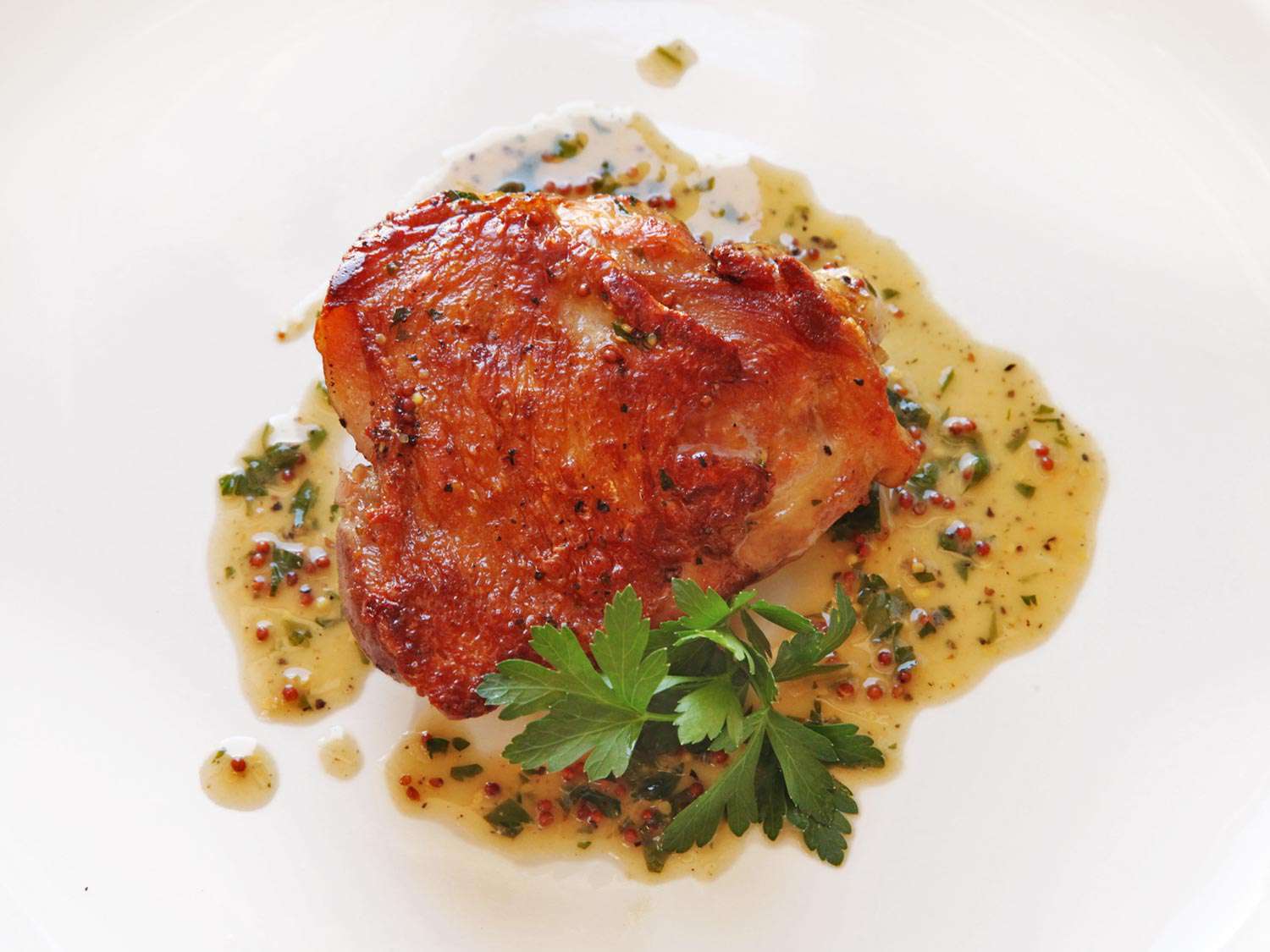 A crispy sous-vide chicken thigh on a plate with a pan sauce. 