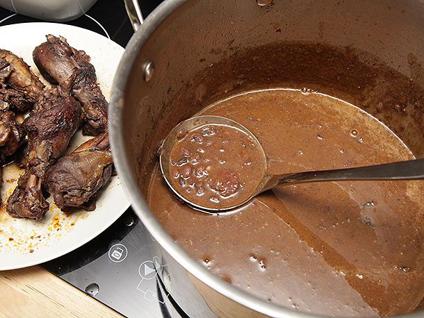 Using a ladle to scoop out black bean soup from a stock pot. Braised chicken is on a plate in the background.