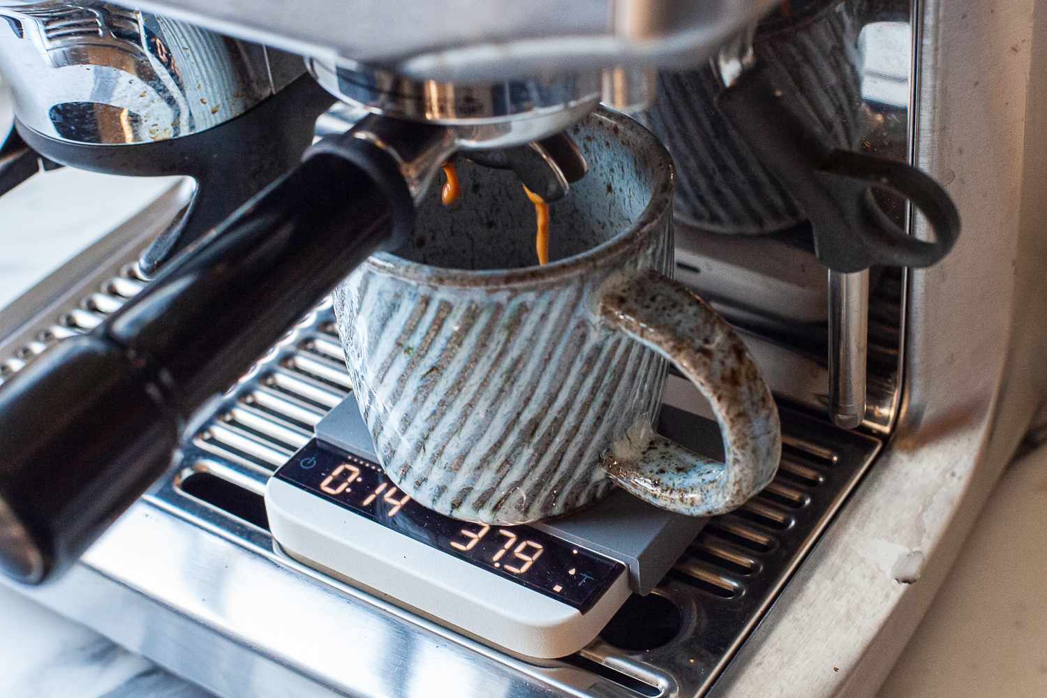 A cup placed under an espresso machine spout, with liquid coffee being dispensed into it on top of Acaia Lunar Scale