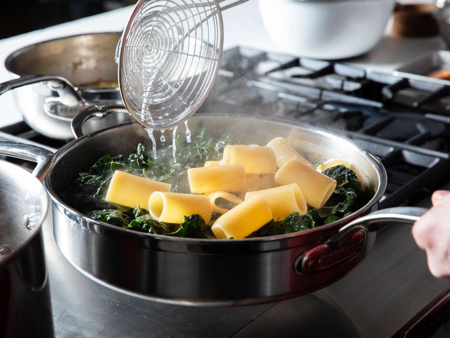 A spider putting some pasta and greens into a shallow pan. 