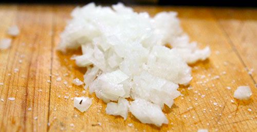 A pile of salted, diced onion on a cutting board.