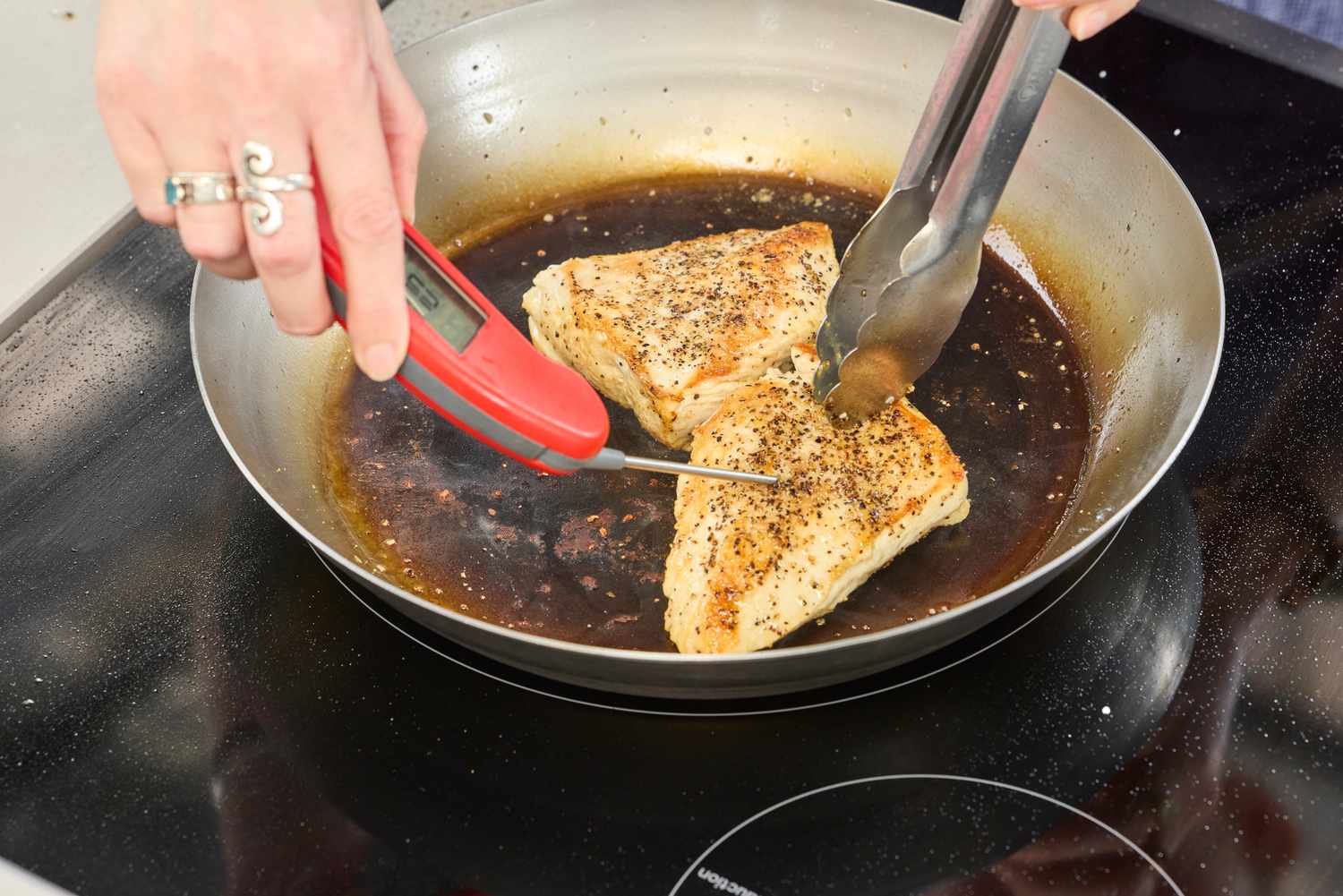 A person checks the temperature of chicken cooking in the Vollrath 12.5 Inch French Style Carbon Steel Fry Pan