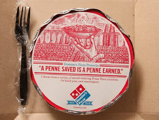 A delivery container from Domino's - a round aluminum dish with a cardboard top and aluminum edges crimped over it. A plastic fork is also in the box. 