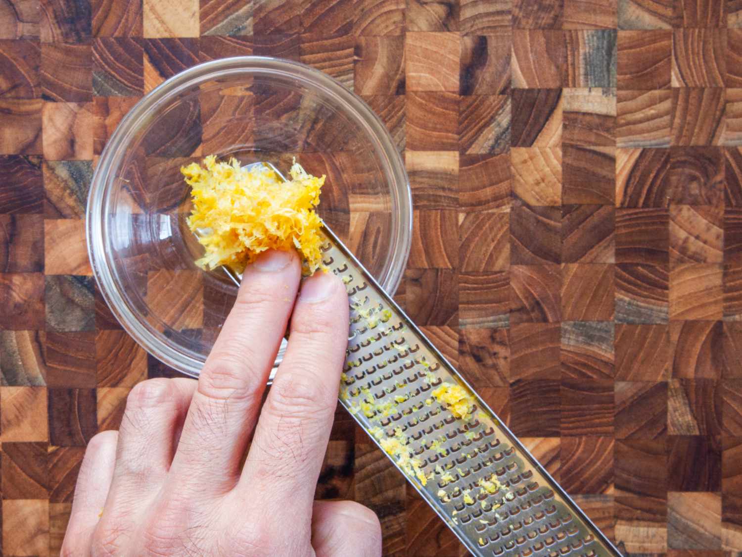 pushing the zest from the bottom of a grater in a small prep bowl