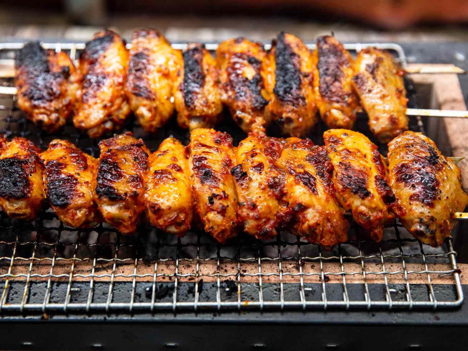 Skewers of grilled Turkish chicken wings on wire rack over charcoal.