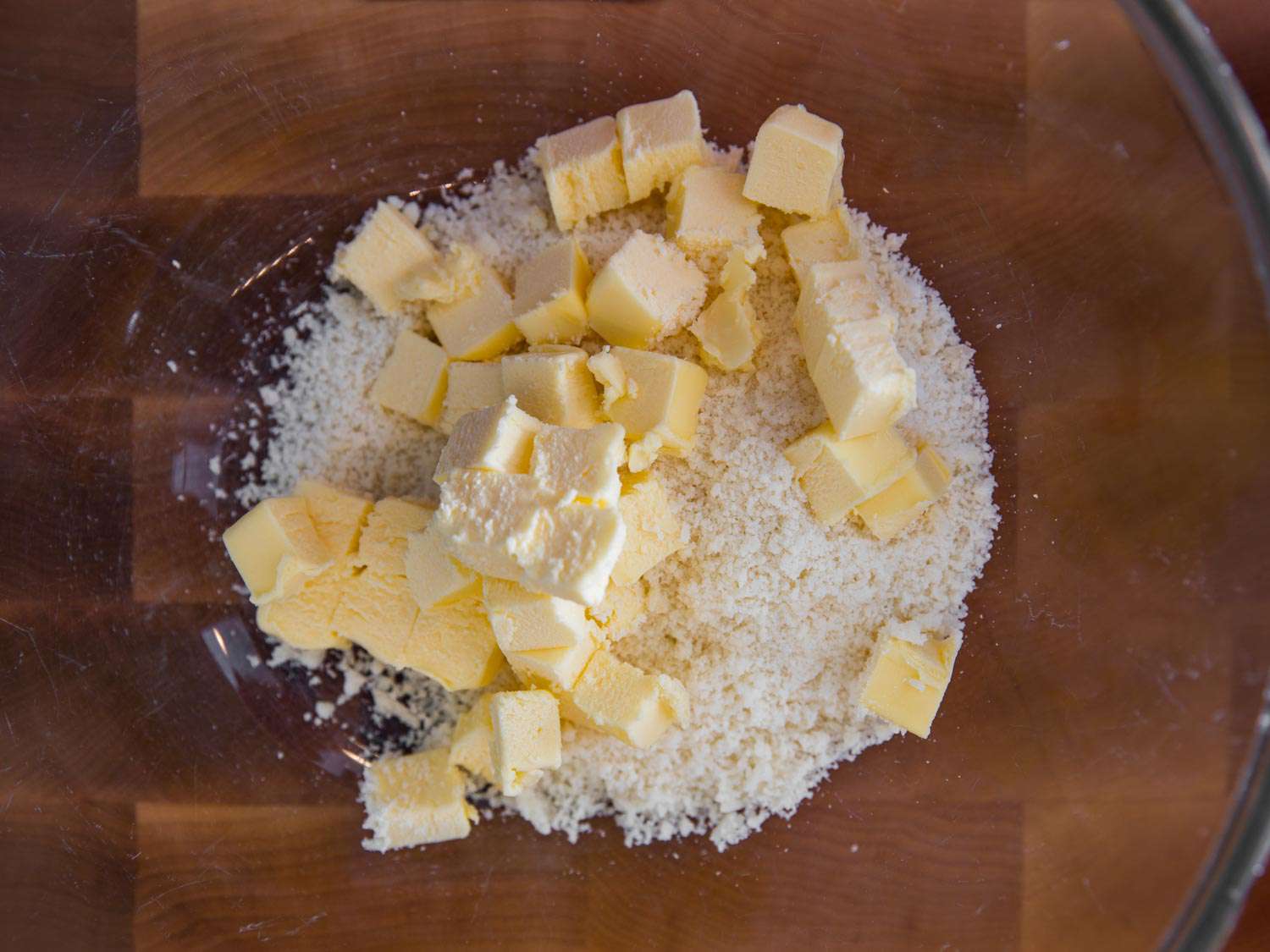 Cubes of butter mixing with grated Parmigiano-Reggiano cheese on a wooden cutting board. 