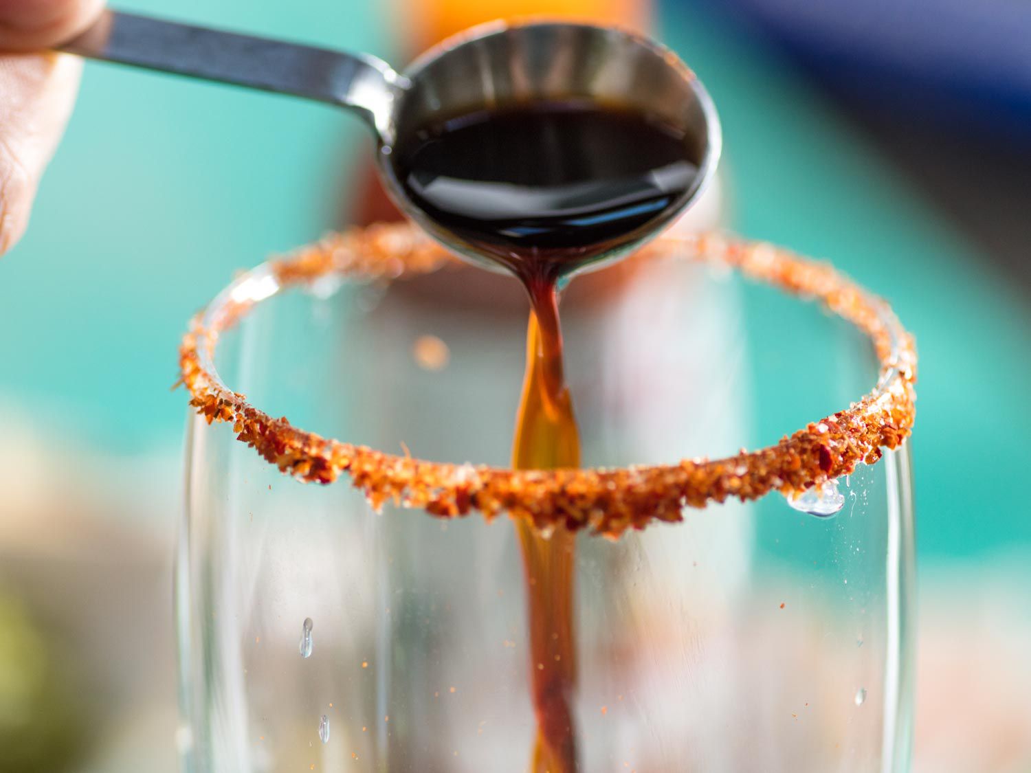 Pouring Worcestershire sauce into a Tajín-rimmed glass for a michelada.
