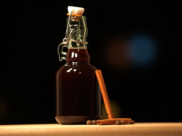 A bottle of allspice dram with allspice berries and cinnamon sticks.