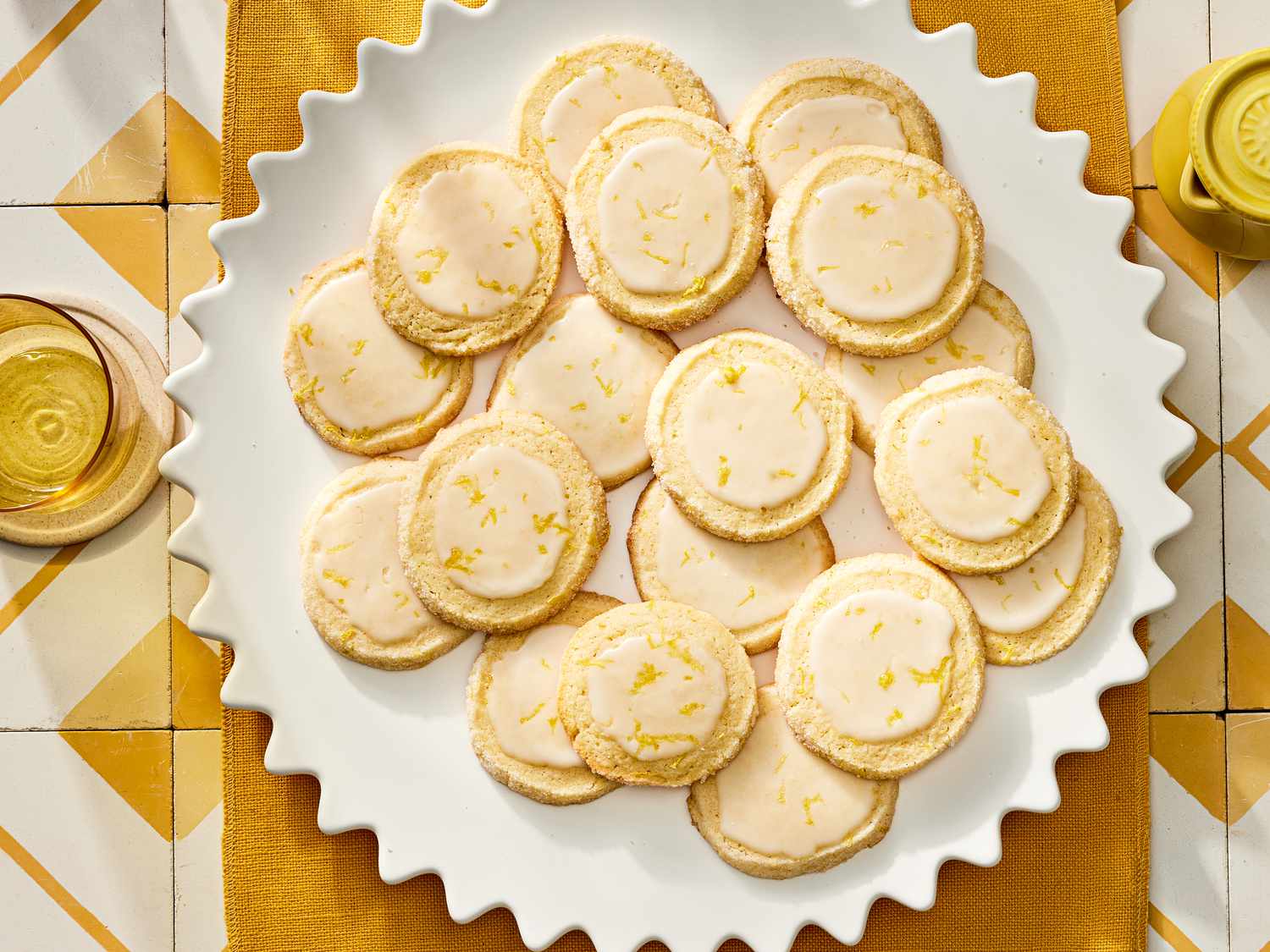 Plate of lemon sugar cookies on a yellow textile on top of yellow and white tiles. 