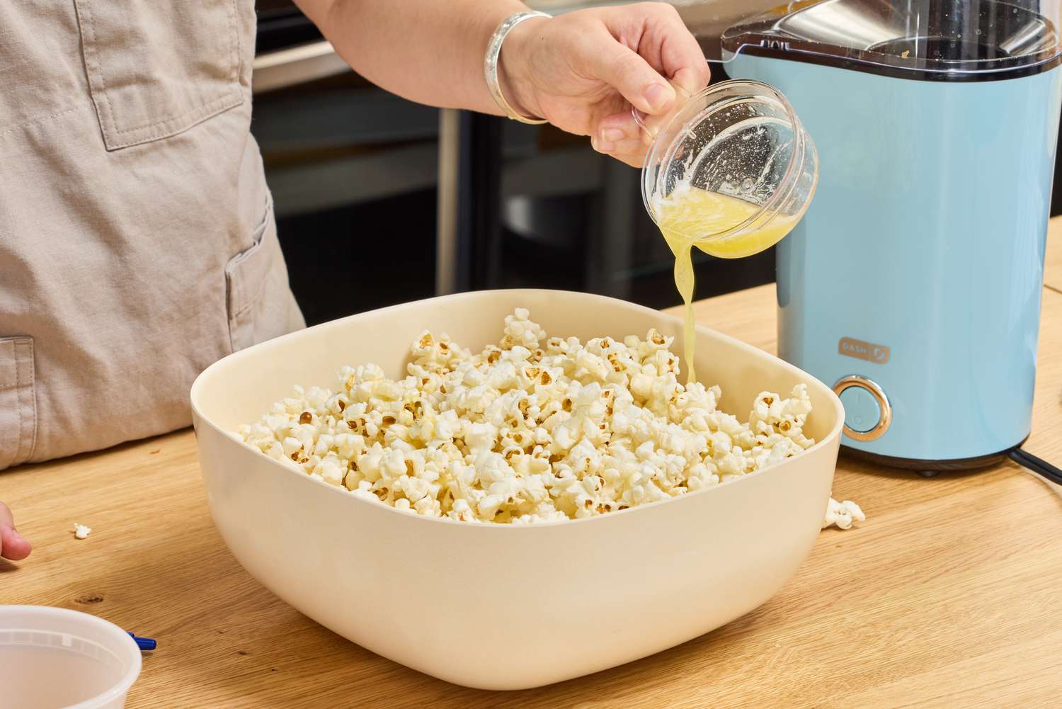 A person pours butter over popcorn made in the Dash Hot Air Popcorn Maker
