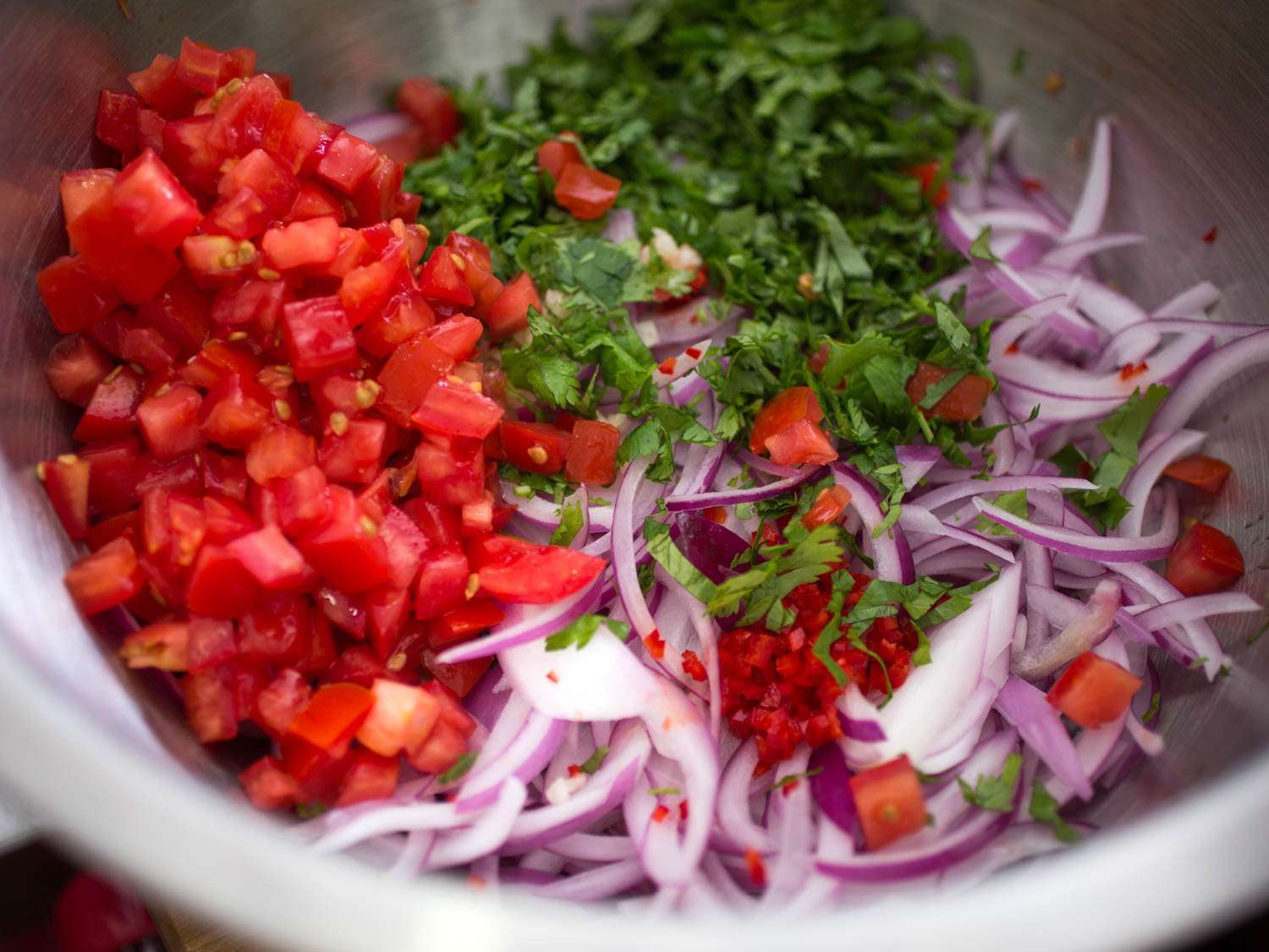 Sliced red onion, chopped tomatoes, chiles, and cilantro in bowl
