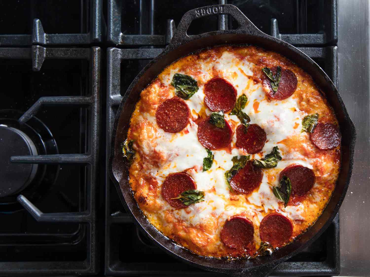 Overhead photo of pan pizza covered in cheese, pepperoni, and basil. 