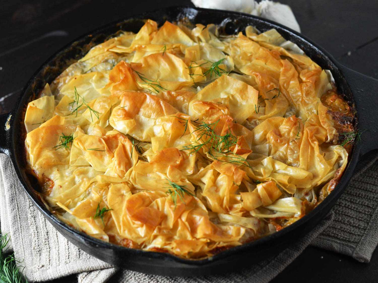 Skillet chicken spinach spanakopita, just out of the oven in a cast iron skillet with golden-brown phyllo and fresh dill on top.