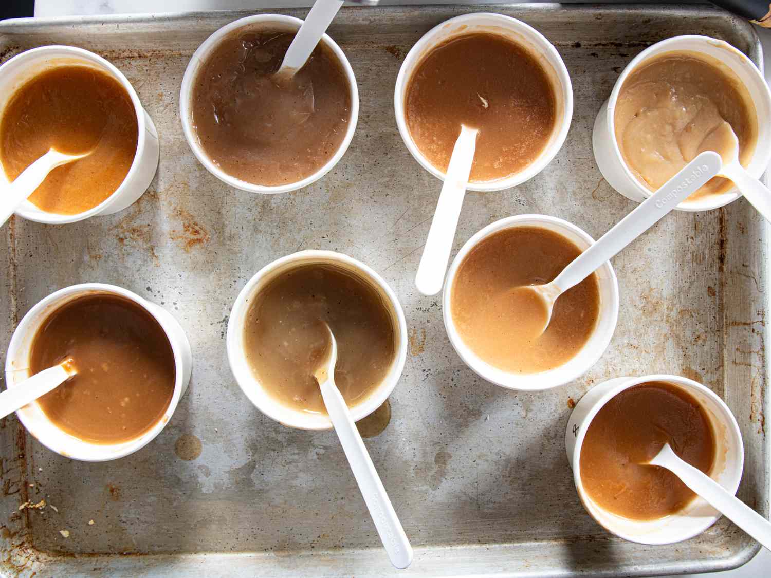 Multiple cups of gravy with spoons on a tray