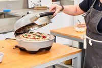 A person closing the lid of the Breville pizza maker.