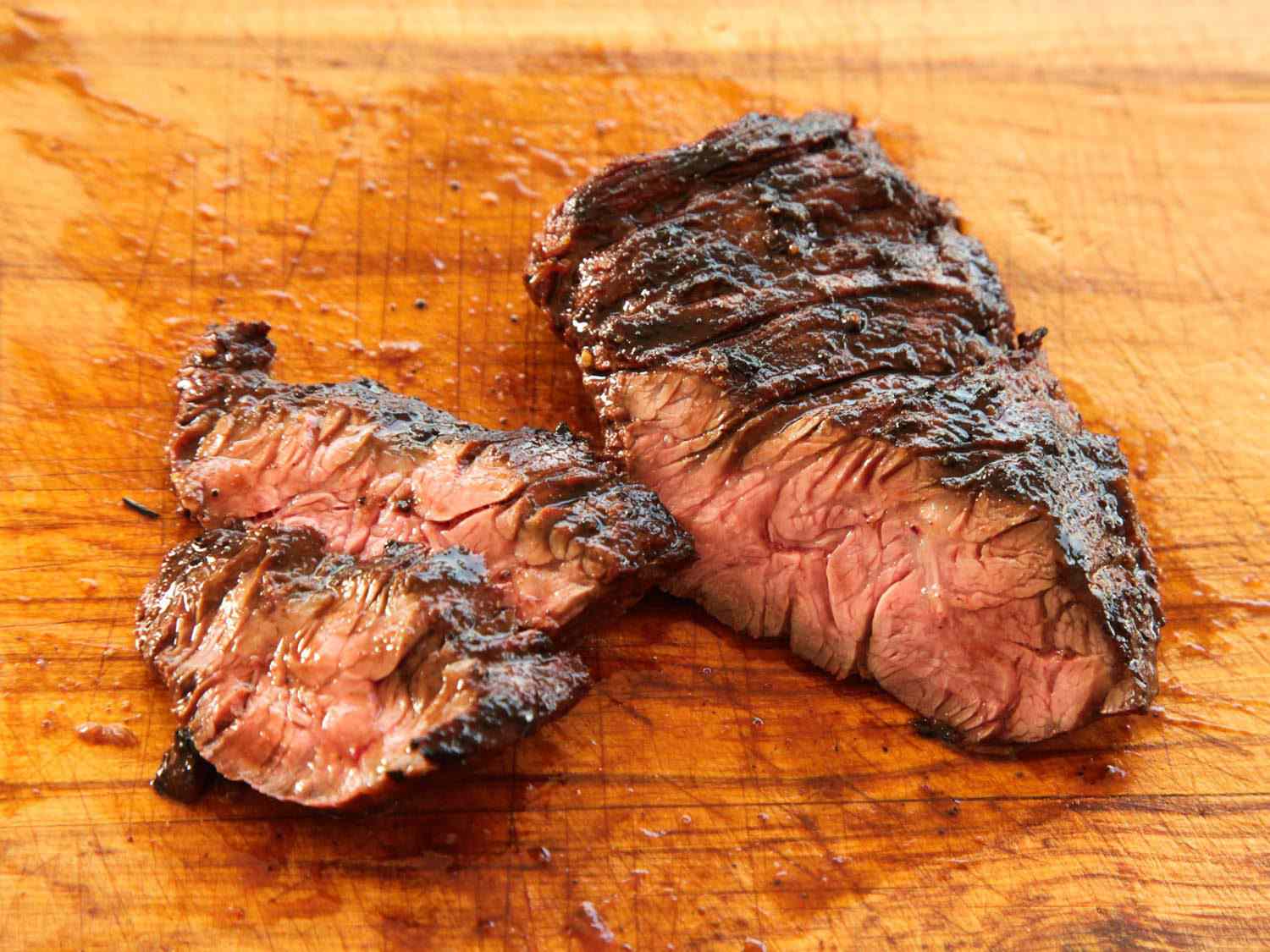 Sliced cooked marinated skirt steak against a wooden cutting board.