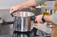 A person places the IMUSA 7 Quart Stovetop Aluminum Pressure Cooker onto a stovetop