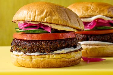 Falafel burgers with tomato cucumber pickled onions and spread on buns displayed on a table