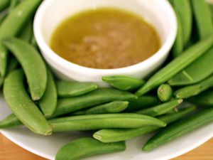A bowl of anchoïade surrounded by sugar snap peas. 