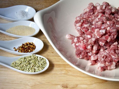 The ingredients for making spicy salsiccia, assembled in a bowl and several porcelain soup spoons.