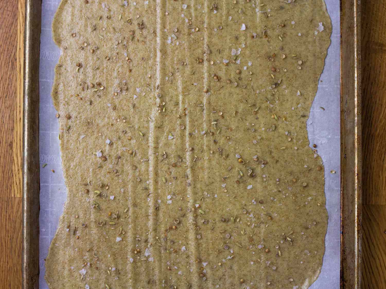  A sheet of thinly rolled out cracker dough on a parchment-lined rimmed baking pan.